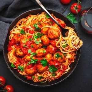 Italian spaghetti pasta in marinara sauce with meatballs, black table background, top view